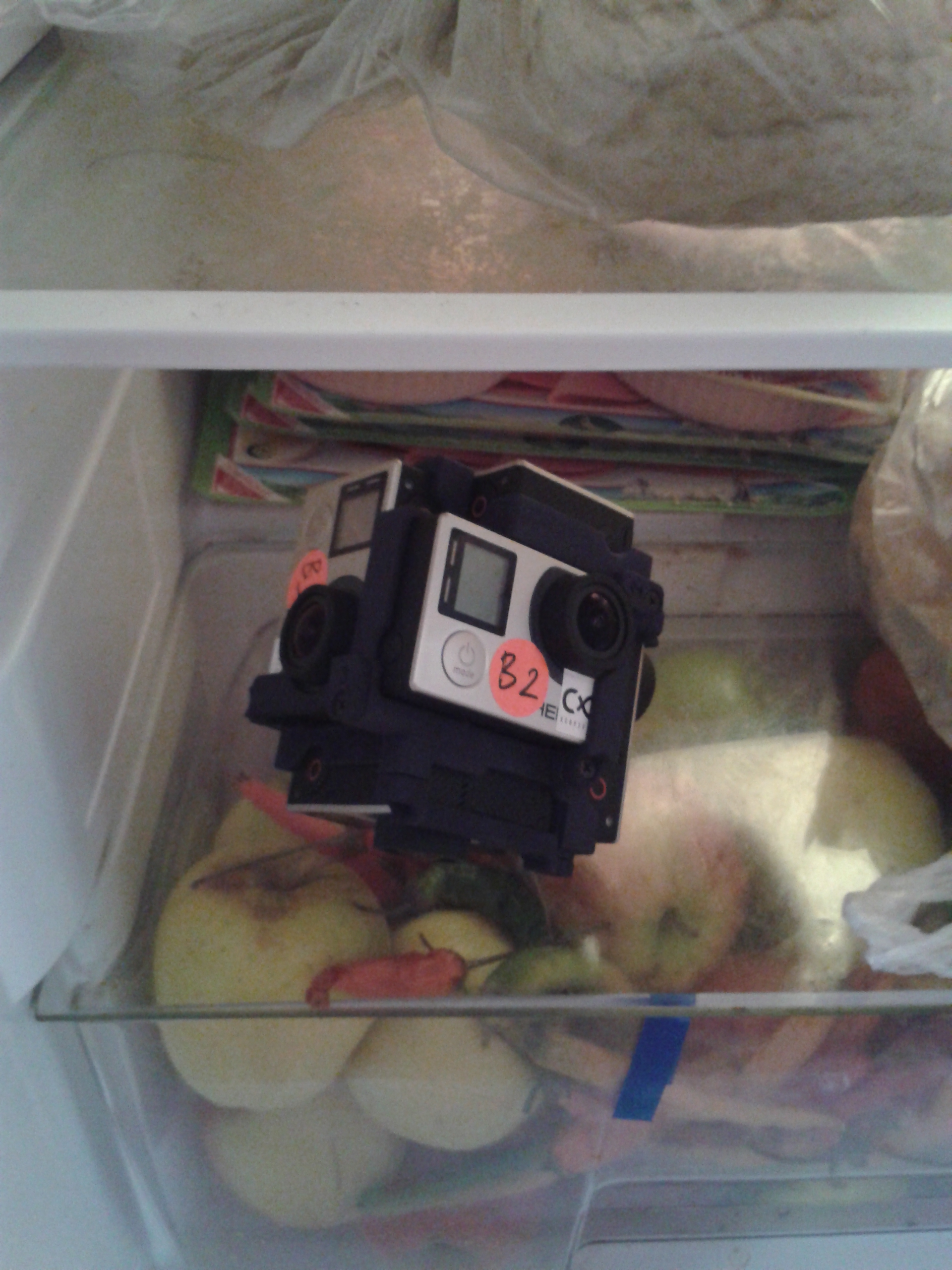 De kubus met GoPro-camera's ligt om af te koelen op de glasplaat boven de groentenla in de koelkast.